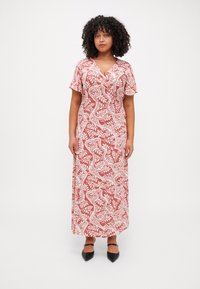 Maxi dress in red with white floral pattern, short sleeves, and a V-neck. Made from lightweight fabric with a flowing design. Black pointed shoes.