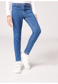 Smala blå denimjeans med en midja av vanlig höjd, med en klassisk femficksdesign och en mjuk textur, kombinerade med vita kardborresneakers.