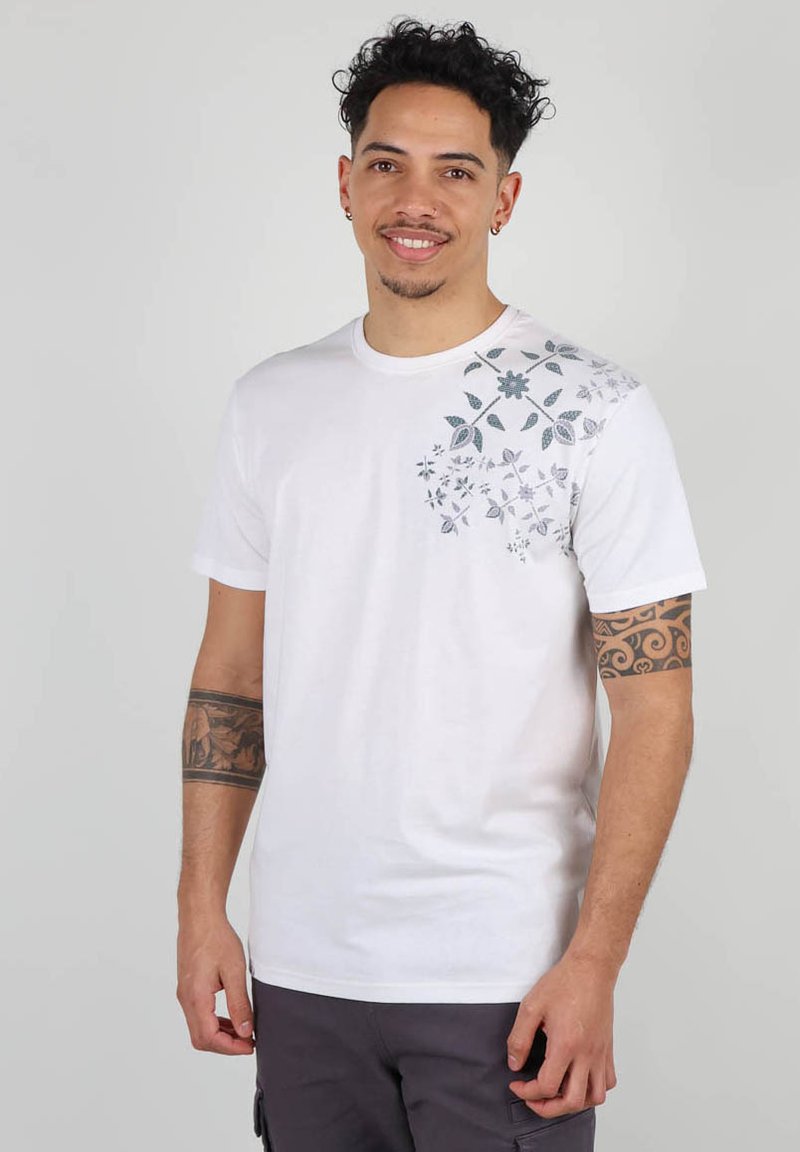 T-shirt en coton blanc avec un motif floral gris et bleu sur le côté supérieur gauche. Manches courtes et col rond.
