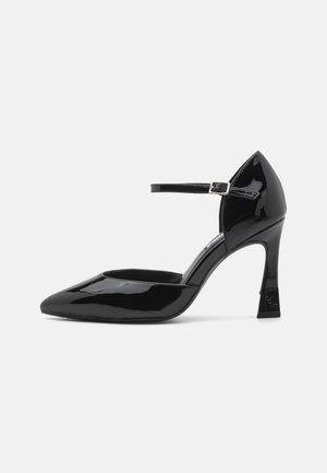 Black patent leather high-heeled shoe with a pointed toe and ankle strap, featuring a square heel and smooth shiny texture.