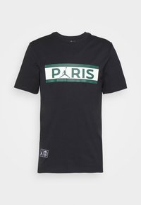 Svart bomullströja med en stor vit och grön grafisk text som säger "PARIS" med en Jumpman-logotyp ovanför och en logotyplapp på sidan.
