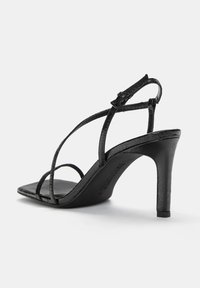 Sandalele cu toc negre au un upper din piele texturată, curele subțiri, vârf pătrat și un toc stiletto zvelt. Include o curea ajustabilă pentru gleznă.