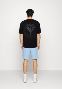Sort kortærmet t-shirt med et stort gråt grafisk design på ryggen, parret med lyseblå shorts og hvide sneakers.