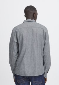 Camisa de manga larga a rayas grises con cuello abotonado, hecha de una tela texturizada, con puños abotonados y dobladillo recto.