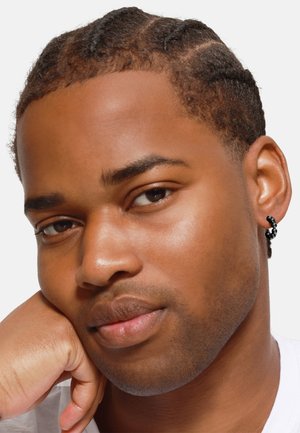 Créole noire scintillante avec un design tordu unique, portée sur une peau lisse et bronzée, mettant en valeur un look propre et naturel.