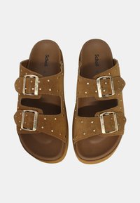 Sandali aperti in suede marrone con due cinturini regolabili dotati di fibbie argento e dettagli in borchie, con una suola marrone imbottita.