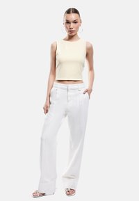 Crème cropped tanktop gecombineerd met hoge witte wijde broek met zijnaad en opgerolde manchetten. Model draagt sleehakken.