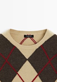 Pull en maille à motif argyle beige et marron avec des accents rouges. Présente un col rond côtelé et une texture douce. Étiquette de marque visible.