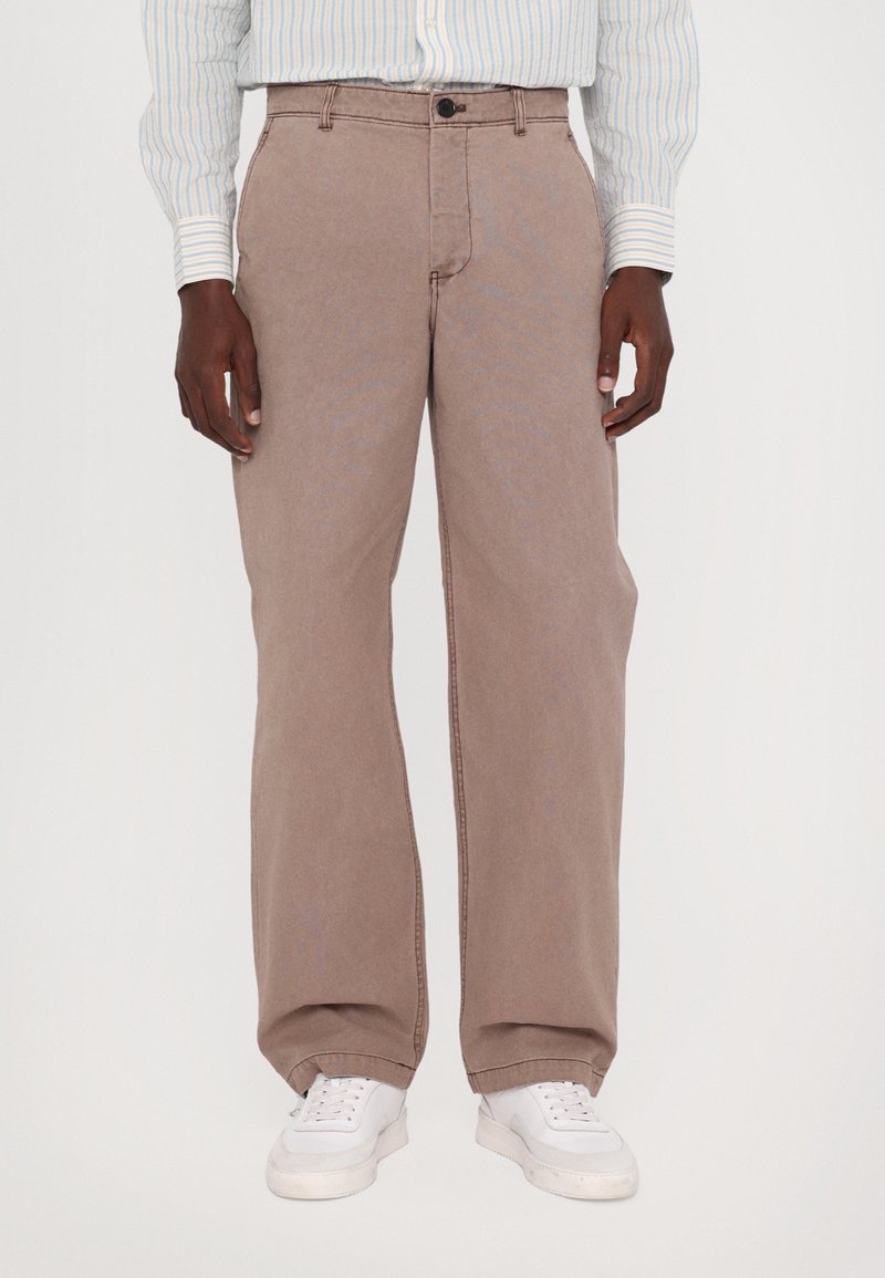 Brown wide-leg pants with a smooth texture, featuring a button closure and belt loops. Styled with white sneakers and a blue-striped shirt.