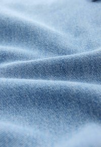 Világoskék denim anyag sima textúrával és finom halszálkamintával, közeli nézetben a szövéssel és a rostokkal.
