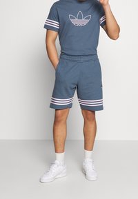 Šedé bavlněné tričko s růžovým logem, spárované se šedými šortkami se růžovými pruhy na spodním okraji. Nosené s bílými teniskami a kotníkovými ponožkami.