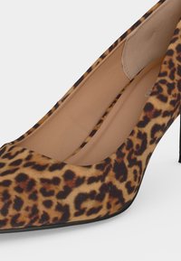 Κοντινή εικόνα ενός ψηλοτάκουνου παπουτσιού με μυτερή μύτη και ύφασμα με λεοπαρτί σχέδιο και μπεζ εσωτερική σόλα πάνω σε λευκό φόντο.