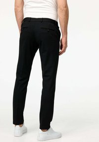 Pantaloni neri con una vestibilità su misura, dotati di passanti per la cintura e due tasche posteriori. Abbinati a sneakers bianche per un look casual.