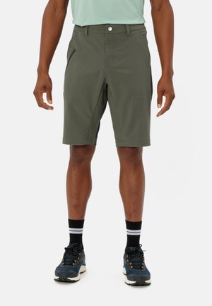 Herren Shorts in Olivgrün aus einem leichten, dehnbaren Stoff. Mit seitlichen Reißverschlusstaschen und einem klassischen Schnitt, kombiniert mit sportlichen Schuhen und Socken.