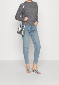 Maglione grigio a maglia, jeans slim azzurri chiari, sandali argentati con tacco quadrato, e una piccola borsa a secchiello argentata con tracolla.
