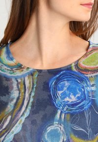 T-shirt in cotone multicolore con scollatura tonda, modelli astratti blu e verdi, e una texture morbida su uno sfondo scuro.