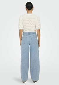 Haut blanc à manches courtes avec un motif perforé, associé à un jean large bleu clair avec une texture florale subtile. Vue arrière.