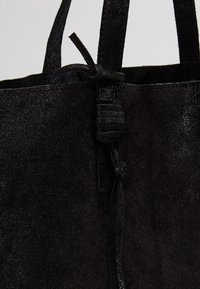 Sac cabas en daim noir avec une fermeture à cordon noué près du haut et deux fines bretelles épaules.