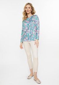 Blomstret langærmet top i turkis, lilla og pink, parret med beige slim-fit bukser og lyse beige flade sko med accent.