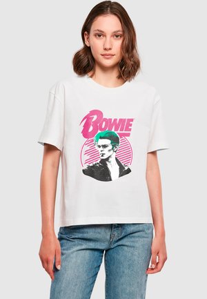 T-shirt blanc à manches courtes avec une impression graphique de David Bowie en noir et teal, avec un texte rose et des rayures circulaires en arrière-plan.