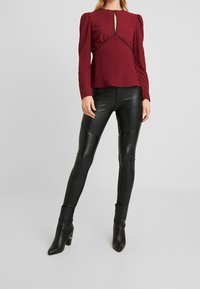 Maglietta bordeaux a maniche lunghe con scollo a chiave, abbinata a leggings in pelle nera aderenti con dettagli a coste e boots alla caviglia.
