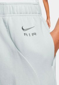 Světle šedé šortky Nike s žebrovanou strukturou, elastickým pasem a vyšitým logem "AIR" se stříbrnými akcenty.