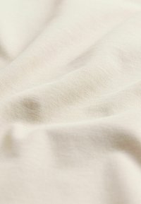 Ljus beige tyg med en slät textur, som har subtila veck och ett fint, vävt mönster. Perfekt för kläder och mjuka möbler.
