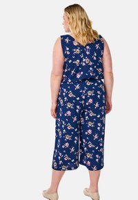 Cvečni kombinezon v mornarici z rožnato in zeleno vzorcem, s brezrokavnim dizajnom in skrajšanimi širokimi hlačami. Gladka tekstura tkanine.