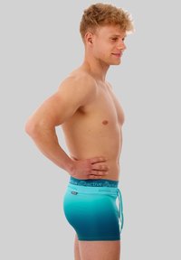 Aqua gradient men's swim trunks with a drawstring waist and logo waistband. Smooth, stretchy material, fitted design, mid-thigh length.