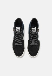 Sneakers de cano alto com uma mistura de camurça azul marinho e preta, atacadores com padrão, sola de borracha branca e um logótipo da marca em destaque na lingueta.