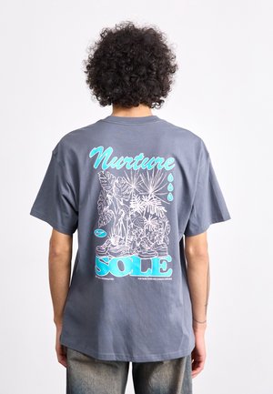 T-shirt en coton gris avec un grand imprimé graphique coloré au dos représentant des plantes tropicales et le texte "Nurture the SOLE."