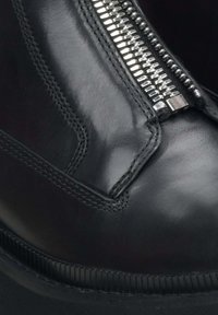 Zwarte leren enkelboot met een zilveren rits, een gladde textuur en contrasterende stiksels langs de naad. De rubberen zool is licht geribbeld.