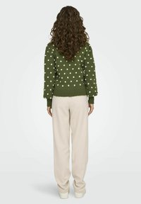 Groene trui met witte stippen, geribde manchetten en zoom, gecombineerd met crème kleurige losse broek en witte sneakers, gefotografeerd van de achterkant.