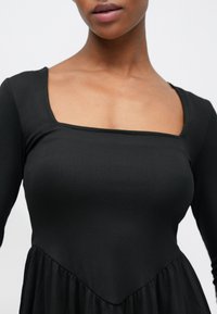 Czarna sukienka z długim rękawem, z prążkowaną fakturą na korpusie, kwadratowym dekoltem i rozkloszowanym dołem z gładkiego, zwiewnego materiału.