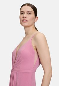 Różowa, bez rękawów sukienka z głębokim dekoltem w literę V i plisowanym wzorem. Wykonana z lekkiego materiału o subtelnym połysku, z przezroczystymi bocznymi panelami.