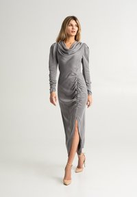 Abito grigio a maniche lunghe con scollatura a cowl, dettaglio arricciato in vita e spacco laterale, realizzato in tessuto morbido con una texture liscia.