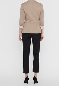 Beżowa dopasowana marynarka z rękawami trzyczwartowymi, białymi mankietami i wyraźnie zarysowaną talią, zestawiona z czarnymi dopasowanymi spodniami i czarnymi szpilkami.