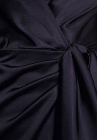Tmavě námořnická látka s záhyby a uzlovým designovým detailem, ukazující hladkou texturu a plynulý splývavý efekt.