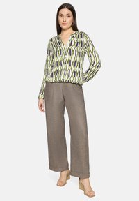 Wzorzysta zielono-biała bluzka z dekoltem w kształcie litery V, zestawiona z luźnymi brązowymi spodniami i jasnobeżowymi sandałami na słupku.