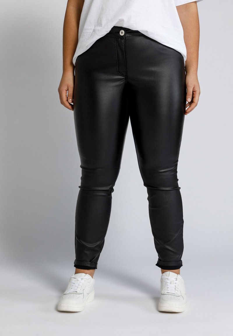 Zwarte faux leren skinny pants met een ritssluiting en knoopsluiting, met een gladde textuur en enkellengte, gecombineerd met witte sneakers.