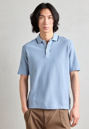 Helles Blaues Polo-Shirt aus strukturiertem Stoff, mit einer Drei-Button-Leiste, kontrastierendem Kragen und kurzen Ärmeln.