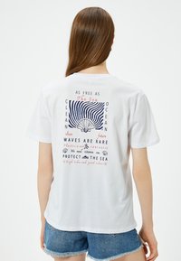 Hvid bomulds T-shirt med et farverigt grafik på ryggen med havrelateret tekst og et skalkoncept, kortærmet og med en afslappet pasform.
