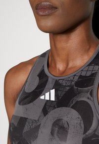Top deportivo sin mangas en gris oscuro con patrones abstractos en negro, que incluye un logo blanco. Textura suave y diseño ajustado, adecuado para ropa deportiva.