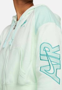 Miętowa bluza z kapturem zapinana na zamek, z teksturowanymi siateczkowymi panelami na ramionach, haftowanym logo "AIR" na rękawie oraz sznurkami przy kapturze.