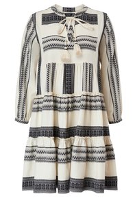 Krämfärgad långärmad klänning i flera lager med svarta geometriska mönster och en knytning med fransar vid halsringningen.