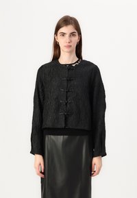 Black cropped jacket with textured fabric, featuring a round neckline, long sleeves, and five toggle fastenings at the front.