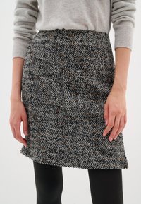 Jupe à motif chevrons en noir, blanc et tons bruns. Fabriquée à partir d'un tissu texturé, elle présente une coupe droite avec un ourlet brut.