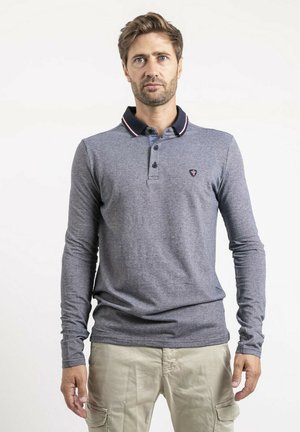 Polo à manches longues bleu marine en tissu texturé, avec un col noir contrastant orné de détails rouges et un petit emblème sur la poitrine.