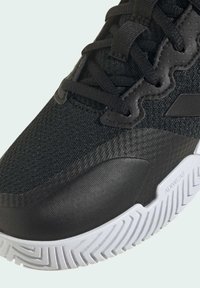 Scarpa sportiva nera con tomaia in mesh testurizzato, accenti sintetici lisci e suola in gomma bianca con un motivo a zigzag.