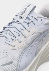 Λευκό αθλητικό παπούτσι με γαλάζια κορδόνια, διχτυωτό επάνω μέρος, παχιά σόλα και ετικέτα «Magnitude 3» στη γλώσσα.